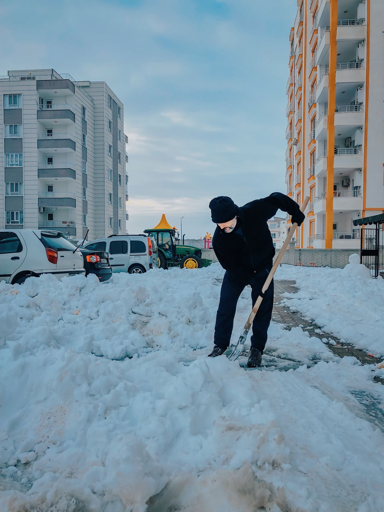 Symbolbild: Person räumt Schnee von einem Gehweg vor Gebäuden