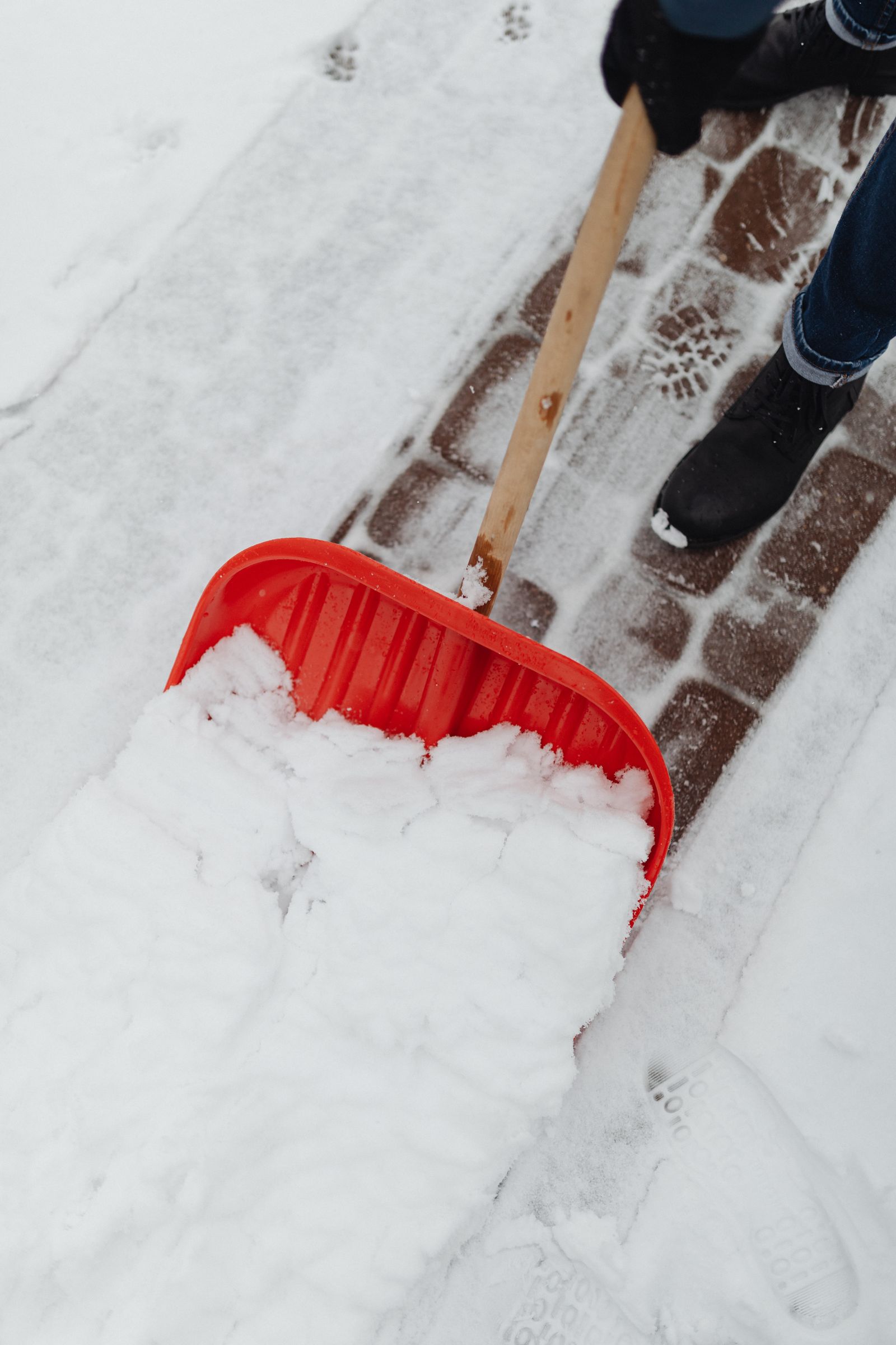 Symbolbild: Person räumt mit einer roten Schneeschaufel einen Gehweg